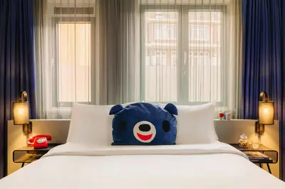 a blue teddy bear sitting on top of a bed at Leonardo Hotel Amsterdam Leidse Square in Amsterdam