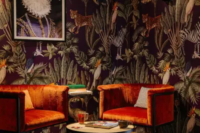 two chairs and a table in a room with a wallpaper at Leonardo Hotel Amsterdam Leidse Square in Amsterdam