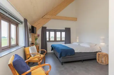 a bedroom with a bed and two chairs and a window at De Groene Bollenschuur in Hillegom