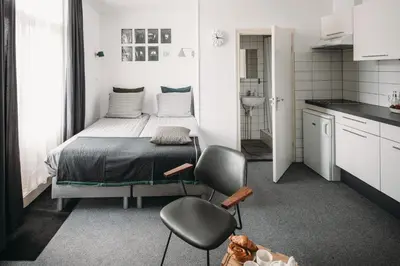 a bedroom with a bed and a chair and a kitchen at Kranenbergh Boutique Apartments in Bergen