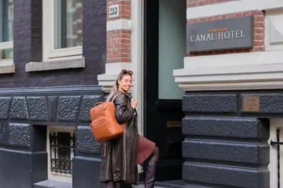 a woman with a orange bag standing outside a building at Amsterdam Canal Hotel in Amsterdam