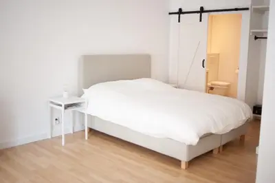 a white bedroom with a white bed and a wooden floor at Achter de duinen in Zandvoort