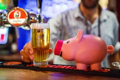 a man holding a glass of beer next to a pig toy at Flying Pig Uptown in Amsterdam