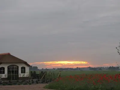 a house in a field with a sunset in the background at Mariahoeve-Logies #Veenhuisje in Woubrugge