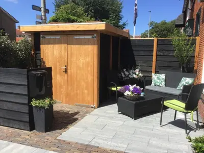 a patio with a wooden shed with a couch and chairs at Sunny dunes in Zandvoort