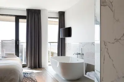 a white bathroom with a tub in front of a bed at Maris Apartments in Egmond aan Zee