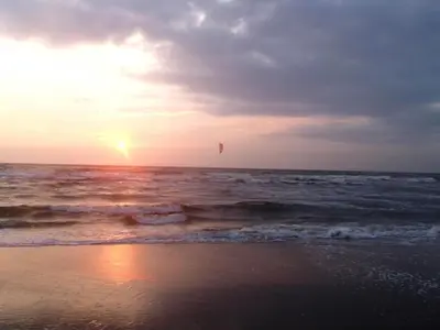 a kite flying over the ocean at sunset at De Specht in Bergen