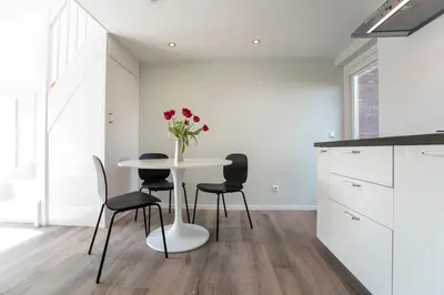 a white kitchen with a table with chairs and a vase of flowers at New Point in Zandvoort