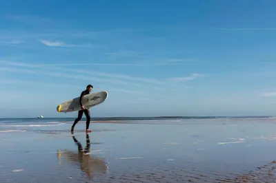 a man walking on the beach with a surfboard at Hotel de Baak Seaside in Noordwijk aan Zee