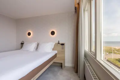 a bedroom with a bed and a large window at Hotel de Baak Seaside in Noordwijk aan Zee