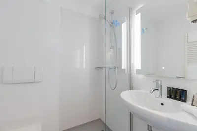 a white bathroom with a shower and a sink at Hotel de Baak Seaside in Noordwijk aan Zee