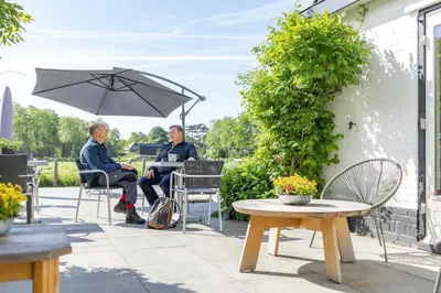 two people sitting on a patio under an umbrella at Villa de Hazelaar in Schoorl