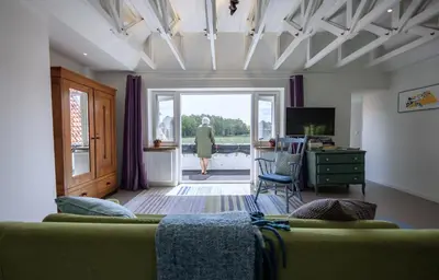 a living room with a green couch and a woman walking out the door at Villa de Hazelaar in Schoorl