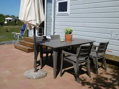 a table with chairs and an umbrella on a patio at Chalet Joleen IJmuiden aan zee, vlakbij het strand in IJmuiden