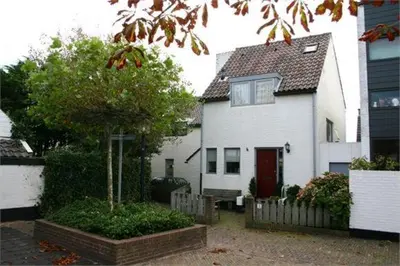 a white house with a red door and a tree at Continentaiz Appartement in Zandvoort