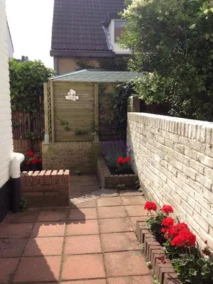 a garden with red flowers and a brick wall at Continentaiz Appartement in Zandvoort