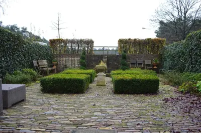 a garden with hedges and a stone walkway at Veld en Bosch in Leusden