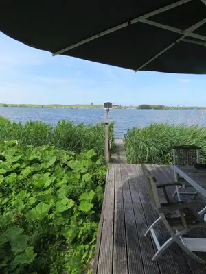 a wooden deck with a table and chairs on the water at Vakantiehuis aan De Mooie Nel in Spaarndam