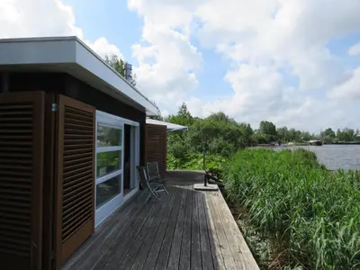 a cabin with a deck next to a river at Vakantiehuis aan De Mooie Nel in Spaarndam