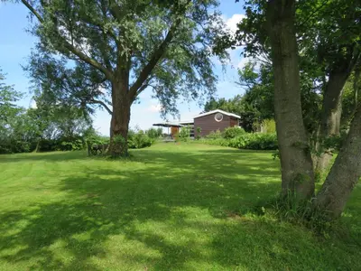 a yard with trees and a house in the background at Vakantiehuis aan De Mooie Nel in Spaarndam
