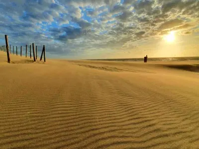 a person standing on a sandy beach with the sunset at Holiday Home in Noordwijk near the Beach in Noordwijk