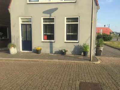 a white house with a blue door and potted plants at De Nollen in Egmond aan den Hoef