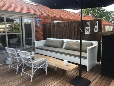 a couch on a deck with chairs and an umbrella at Bergenshofje in Bergen