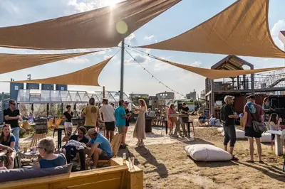 a group of people on the beach under a large umbrella at Basecamp Tiny House Eco-resort IJmuiden in IJmuiden