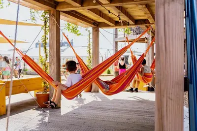 a boy sitting in a hammock on a dock at Basecamp Tiny House Eco-resort IJmuiden in IJmuiden