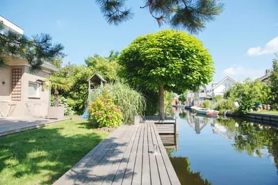 a wooden walkway next to a river with a tree at Luxury villa on peaceful location. Boat optional in Vinkeveen