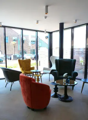 a lobby with chairs and tables and windows at Blue Mansion Hotel in Aalsmeer