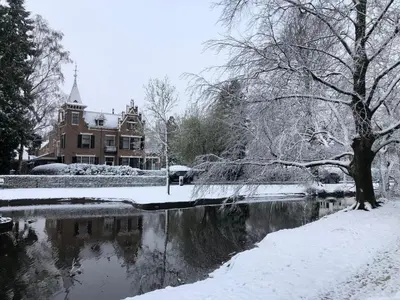 a house in the snow next to a river at Modern Palace Emma Staete in Baarn