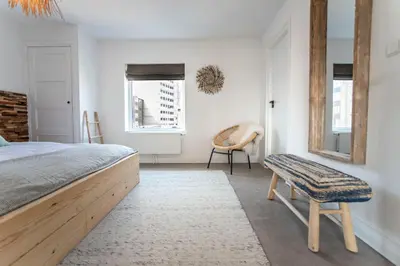 a bedroom with a bed and a chair and windows at Bamboa Beachhouse in Zandvoort