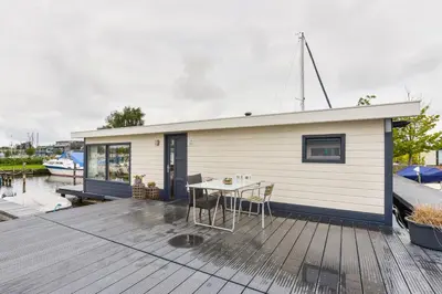 a small house with a table on a wooden deck at Bright and Comfortable Houseboat in Aalsmeer