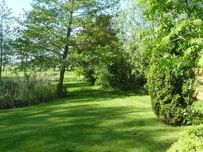 a garden with green grass and trees and bushes at Bed & Breakfast De Koegang in Zuidermeer
