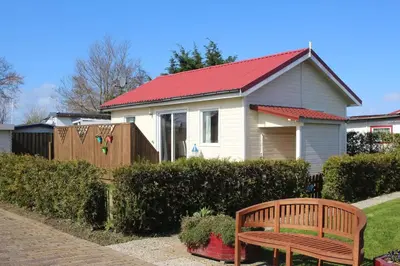 a house with a red roof and a wooden bench at Haus zum Leuchtturm Ferienpark Vislust Niederlande Ijsselmeer in Wervershoof