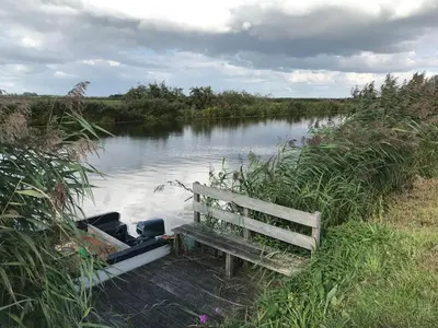 a bench sitting next to a river with a boat at Aan de Wiericke in Driebruggen
