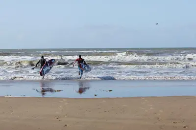 two people walking into the ocean with their surfboards at Center Parcs Zandvoort beach in Zandvoort