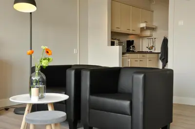 a living room with a black leather chair and a table at Residence Le Mistral in Noordwijk aan Zee