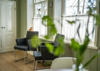 a waiting room with chairs and a table and windows at Traditional family apartment with garden at countryside Amsterdam in Landsmeer
