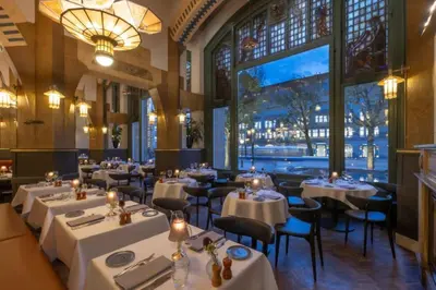 a restaurant with white tables and chairs and a large window at Clayton Hotel Amsterdam American in Amsterdam
