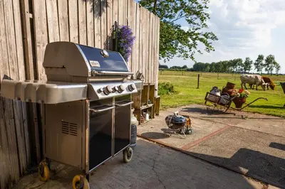 a grill sitting next to a fence next to a field at Bed&Bbq Longhornranch in Akersloot