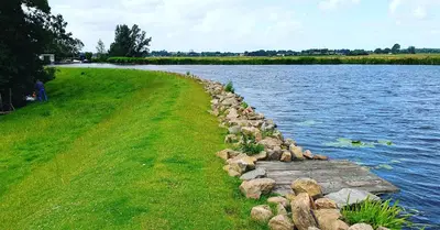 a rock retaining wall next to a body of water at Lake house 21 relax accommodation iR Sauna in Warmond