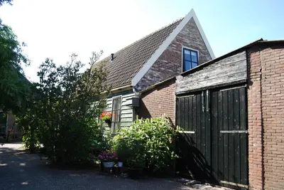 a brick house with a black garage and a tree at Bed&Brood De StraVerdonk in Graft
