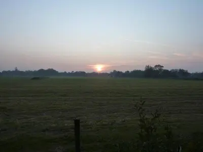 a field with the sun setting in the horizon at Eureka Vakantiehuisjes in Schoorl
