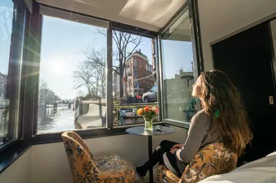 a woman sitting in a chair looking out of a window at 2 Houseboat Suites Amsterdam Prinsengracht in Amsterdam