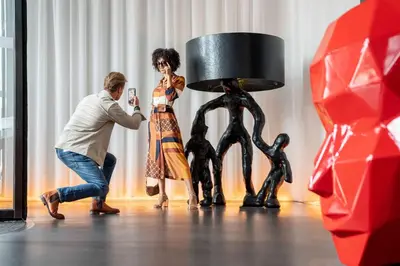 a man taking a picture of a woman standing next to a statue at art'otel amsterdam, Powered by Radisson Hotels in Amsterdam