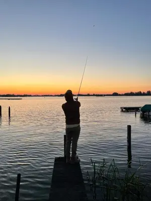 a person standing on a dock fishing on a lake at The Outpost Lakehouse- enjoy our house at Reeuwijkse Plassen - near Gouda in Reeuwijk