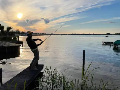 a man standing on a dock fishing on a lake at The Outpost Lakehouse- enjoy our house at Reeuwijkse Plassen - near Gouda in Reeuwijk