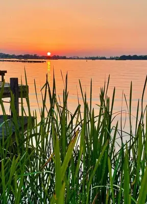 a sunset over a body of water with grass at The Outpost Lakehouse- enjoy our house at Reeuwijkse Plassen - near Gouda in Reeuwijk